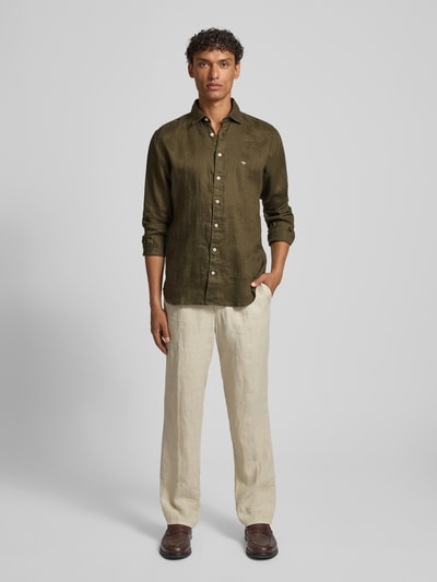 Mężczyznamodel nosi Slim Fit Leinenhemd mit Haifischkragen von Fynch-Hatton, len, krój slim fit, wyhaftowane logo, kołnierzyk typu cutaway, długość tyłu w rozmiarze M: 77 cm, szerokość ramion w rozmiarze M: 47 cm, długość rękawów w rozmiarze M: 61 cm, oliwkowy kolor, gładka tekstura, widok całej sylwetki z przodu