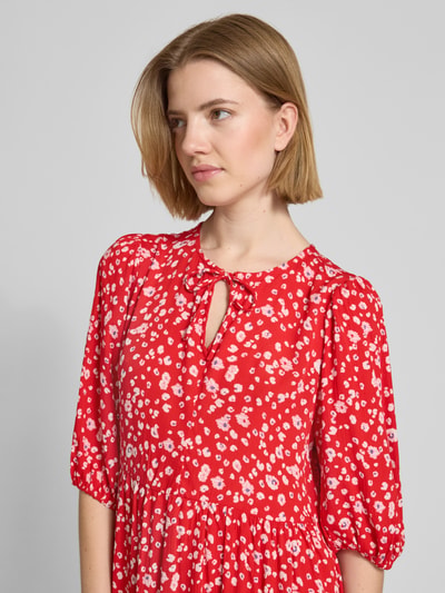 Frauenmodel trägt Minikleid aus Reine Viskose im Allover-Look Modell 'MARRAKECH' von ICHI, A-Linie, Nahaufnahme Oberkörper. Rückenlänge 34 cm, Brustweite 35 cm, Ärmellänge 37 cm bei Größe S, rote Grundfarbe mit weißem Muster, glatte Textur.