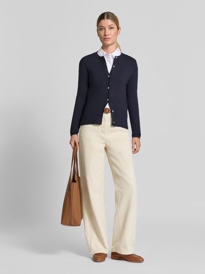 Vrouwenmodel draagt Regular Fit gebreid jack uit Viscosemix met geschulpte zoom van Christian Berg Woman, Dames, knoopsluiting, lange mouw, ribboorden, ruglengte maat S 56 cm, mouwlengte S 61 cm, donkerblauw, lichte broek, bruine tas en schoenen, full-body vooraanzicht.