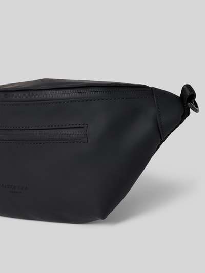 Produktfoto, schwarze Bauchtasche mit Logo-Detail Modell 'SPLÄSH BUMBAG' von GASTON LUGA, glatte Textur, Reißverschluss, neutraler Hintergrund. Hauptfach, verstellbarer Trageriemen, Maße: 32x15x4 cm, Riemenlänge 88 cm.