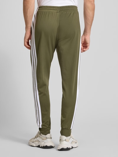 Männermodel trägt Regular Fit Sweat-Anzug mit Kontraststreifen von adidas Sportswear in Oliv mit weißen Kontraststreifen, Ganzkörperansicht Rückansicht.