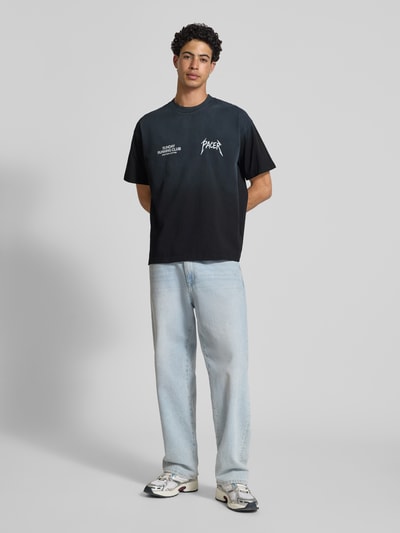 Männermodel trägt T-Shirt mit Statement-Print Modell 'SRC® Pacer' von ANOTHER COTTON LAB, reine Baumwolle, Boxy Fit, Ganzkörperansicht von vorne