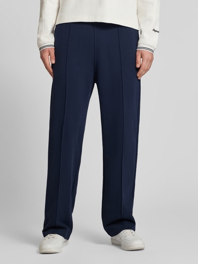 Męski model nosi Sweatpants mit Längsnähten und Label-Stitching von CHAMPION z mieszanki bawełny, krój relaxed fit, elastyczny pas, ciemnoniebieskie, wyhaftowane logo, długość wewnętrzna nogawki w rozmiarze M: 81 cm, całkowity widok z przodu.