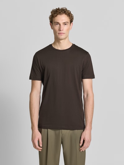Mężczyznamodel nosi T-Shirt aus Baumwolle mit Rundhalsausschnitt von Christian Berg Men, krój slim fit, okrągły dekolt, długość tyłu w rozmiarze M 73 cm, ciemnobrązowy kolor, prosta faktura, widok całej sylwetki z przodu.