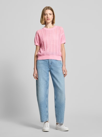 Modelka nosi Relaxed Fit Strick-Shirt aus Baumwoll-Mix Modell 'LUX LIGHT' od Vero Moda, różowy, ażurowy wzór, krótki rękaw, widok całej sylwetki z przodu.