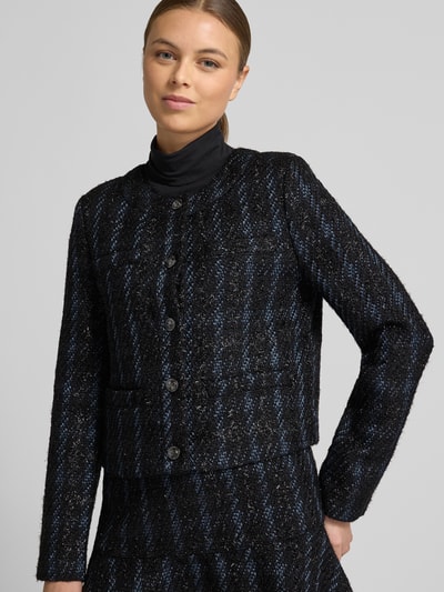 Kobiece modelka nosi żakiet z listwą guzikową model 'ANDIE' od Guess, mieszanka materiałów z dodatkiem streczu, krój regular fit, okrągły dekolt, wpuszczane kieszenie, długość tyłu 53 cm, szerokość klatki piersiowej 45 cm, długość rękawów 62 cm, ciemna tekstura z niebieskimi akcentami, widok na cały przód górnej części ciała.