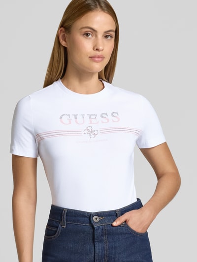 Frauenmodel trägt T-Shirt mit Strasssteinbesatz Modell 'SIENA' von Guess, weiß, Logo-Print, Baumwoll-Mix, Nahaufnahme Oberkörper.