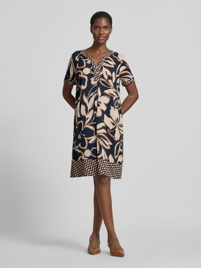 Frauenmodel trägt A-Linien Freizeitkleid aus reiner Viskose von Betty Barclay mit großem floralen Muster in Beige und Dunkelblau, Ganzkörperansicht von vorne.