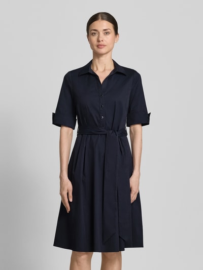 Modelka nosi knielanges Hemdblusenkleid mit Bindegürtel von ROBE LÉGÈRE, bawełniany miks z domieszką stretchu, krój taliowany, długość do kolan, kołnierz koszulowy, krótka listwa guzikowa, pasek do wiązania, rękawy z mankietem, długość tyłu w rozmiarze 36: 104 cm, szerokość w rozmiarze 36: 42 cm, długość rękawa w rozmiarze 36: 30 cm, kolor granatowy, gładka faktura, widok całej sylwetki z przodu.