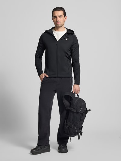 Männermodel trägt Slim Fit Jacke mit Logo-Print Modell 'Rider' von Peak Performance aus Elastischer-Material-Mix, Schwarz, Ganzkörperansicht von vorne.