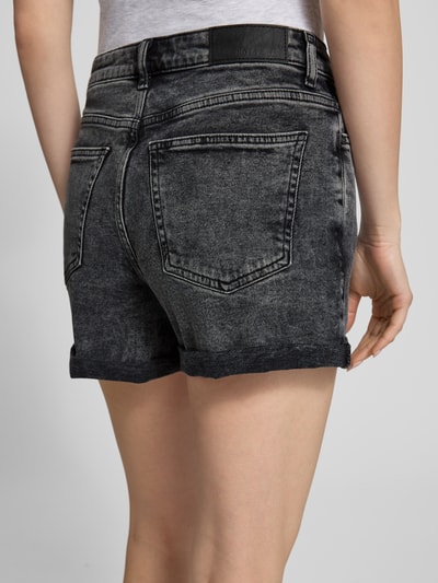 Frauenmodel trägt High Waist Jeansshorts mit Umschlag Modell 'MONI' von Noisy May im Regular-Fit aus Baumwoll-Elasthan-Mix, Eingrifftaschen, Bundweite 38 cm, Innenbeinlänge 9 cm, dunkles Denim, Textur sichtbar, Ganzkörperansicht Rückansicht.