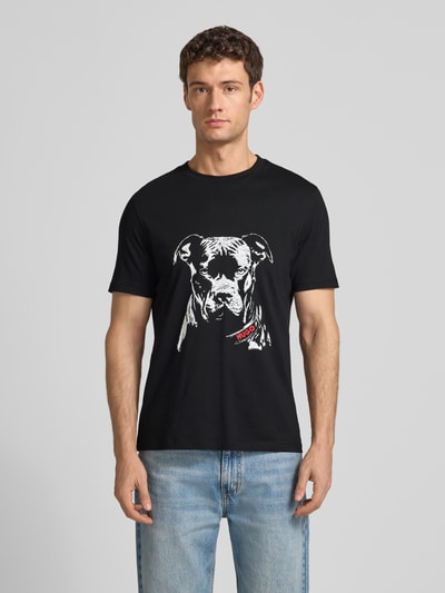 Männermodel trägt Regular Fit T-Shirt aus reiner Baumwolle Modell 'DUBROX' von HUGO in Schwarz mit Motiv-Print, Ganzkörperansicht von vorne.