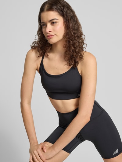 Vrouwenmodel draagt Slim Fit Sport-BH met logo-print van New Balance, elastische materiaalmix, spaghettibandjes, slim fit, logoprint. Nahaufnahme Oberkörper.