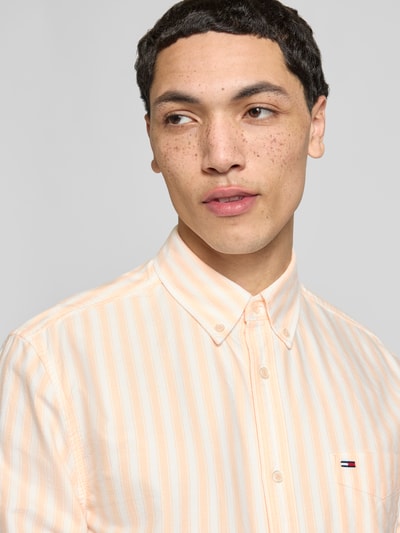 Männermodel trägt Regular Fit Freizeithemd aus reiner Baumwolle von Tommy Jeans mit gelb-weißen Streifen, Logo-Stitching, Nahaufnahme Oberkörper.