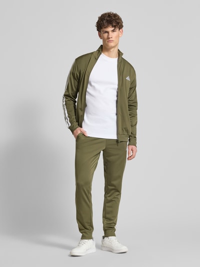 Männermodel trägt Regular Fit Sweat-Anzug mit Kontraststreifen von adidas Sportswear in Olivgrün, Optik: Unifarben, Ganzkörperansicht von vorne.