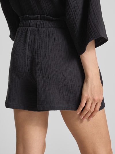 Frauenmodel trägt Loose Fit Shorts aus reiner Baumwolle Modell 'NATALI' von Vero Moda, Optik: Unifarben, Materialverarbeitung: Crêpe, Bundabschluss: elastisch, Eingrifftaschen, Farbe: dunkel, Struktur: leicht gekreppte Oberfläche, Ganzkörperansicht Rückansicht.