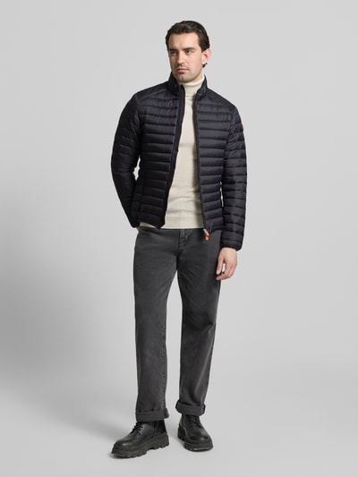 Männermodel trägt Steppjacke mit Zweiwegereißverschluss Modell 'Alexander' von SAVE THE DUCK in Schwarz, Stepp-Optik, Regular Fit, Ganzkörperansicht von vorne.