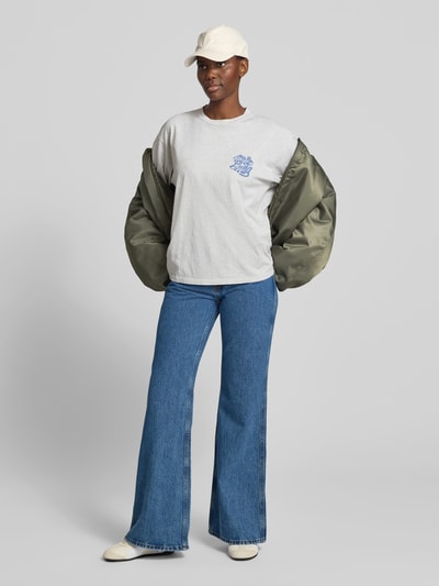 Frauenmodel trägt Flared Fit Jeans im 5-Pocket-Design von Anine Bing aus Reine Baumwolle in mittlerem Blau, Logo-Detail, Knopf-Reißverschluss, Ganzkörperansicht von vorne.