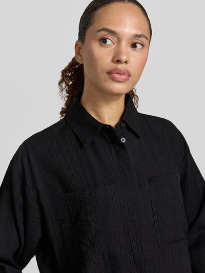 Frauenmodel trägt Regular Fit Bluse aus Viskose-Mix Modell 'Forna' von OPUS, Hemdblusenkragen, verdeckte Knopfleiste, Brusttaschen, 3/4-Arm, schwarze Struktur, Nahaufnahme Oberkörper.