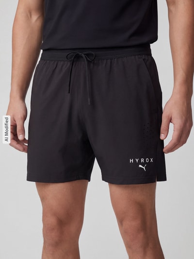 Männermodel trägt schwarze Regular Fit Sportshorts mit Label-Print von PUMA Performance, dezenter Glanz, glatte Textur, Nahaufnahme Oberkörper.