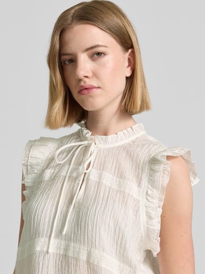 Frauenmodel trägt Regular Fit Bluse aus Viskose-Mix Modell 'Viroeressa' von mbyM mit Rüschenbesatz, Ärmelloses-Design, Stehkragen mit Tunnelzug und Schlüssellochausschnitt, Rückenlänge bei Größe S: 53 cm, Nahaufnahme Oberkörper.