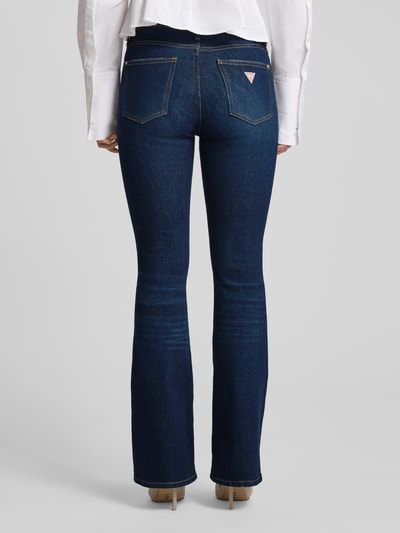 Frauenmodel trägt Flared Jeans mit 5-Pocket-Design von Guess, dunkelblauer Baumwoll-Mix mit Stretch-Anteil, Ganzkörperansicht Rückansicht.