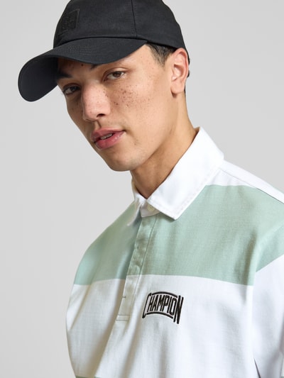 Männermodel trägt Relaxed Fit Poloshirt aus Baumwolle von CHAMPION in Weiß und Mint mit Label-Stitching, Nahaufnahme Oberkörper.