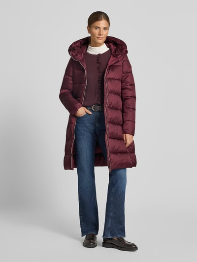 Frauenmodel trägt Steppmantel mit Kapuze Modell 'LYSA' von Save The Duck, bordeaux, gesteppte Struktur, Ganzkörperansicht von vorne. Damen Steppmantel, gerader Schnitt, Zweiwege-Reißverschluss, Label-Patch, seitliche Eingrifftaschen, Rückenlänge 91 cm, Schulterbreite 39 cm, Brustweite 40 cm, Ärmellänge 66 cm.