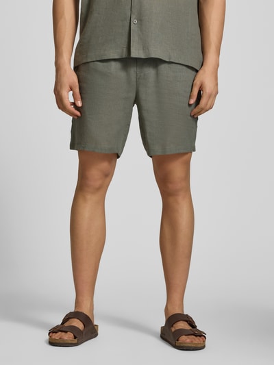 Mężczyzna nosi Regular Fit Shorts aus Leinen-Viskose-Mix Modell 'LAURENCE' od Only & Sons, oliwkowa zieleń, gładka faktura, krój regular fit, elastyczny pas, kieszenie boczne i tylne, widok z przodu, ujęcie całej sylwetki.