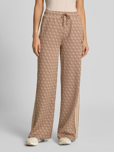 Frauenmodel trägt Sweatpants mit Logo-Muster im Allover-Look von GUESS, Wide Leg, elastischer Bund mit Tunnelzug, Material-Mix mit Stretch-Anteil, beige und creme, Ganzkörperansicht von vorne.
