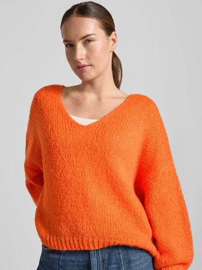 Frauenmodel trägt Oversized Strickpullover mit Mohair-Anteil von Oui in Orange, V-Ausschnitt, grobe Strickstruktur, Nahaufnahme Oberkörper, Damen Strickpullover, Material-Mix, gerippte Abschlüsse, Rückenlänge 37 cm, Ärmellänge 48 cm.