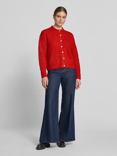 Frauenmodel trägt Relaxed Fit Strickjacke mit Woll-Anteil Modell 'Belablue' von ICHI in Rot, langärmlig, Knopfleiste, Jeans, Ganzkörperansicht von vorne.