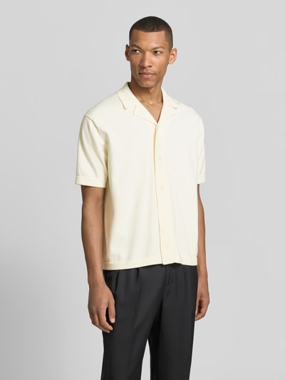 Männermodel trägt Regular Fit Strickjacke aus reiner Baumwolle Modell 'AMOUR' von SELECTED HOMME in Optik: Unifarben, einreihige Knopfleiste, Intarsie, Reverskragen, Kurzarm, Materialverarbeitung: Strick, Farbe: creme, Textur weich, Ganzkörperansicht von vorne.
