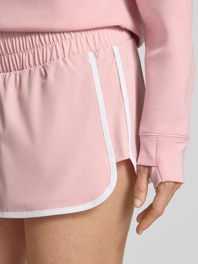 Frauenmodel trägt Running Shorts mit elastischem Bund von VARLEY in Rosa mit weißer Paspel, Material-Mix mit Stretch, Nahaufnahme Oberschenkel.
