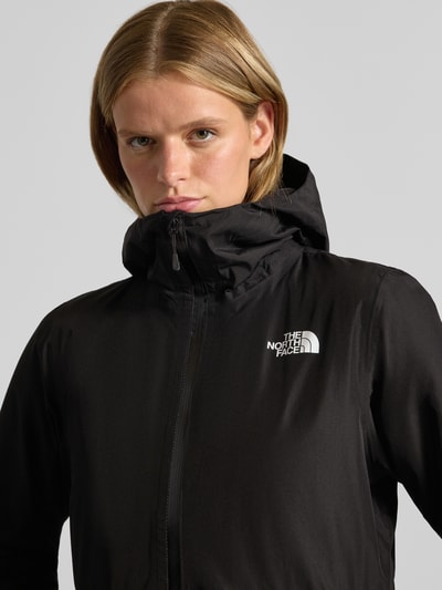 Kobieta nosi czarną kurtkę z kapturem, zamek błyskawiczny dwustronny, logo The North Face, model 'HIKESTELLER', krój regular fit, kieszenie zapinane na zamek błyskawiczny, długość tyłu w rozmiarze S: 86 cm, szerokość ramion w rozmiarze S: 41 cm, szerokość w rozmiarze S: 52 cm, długość rękawów w rozmiarze S: 65 cm, zbliżenie na górną część ciała