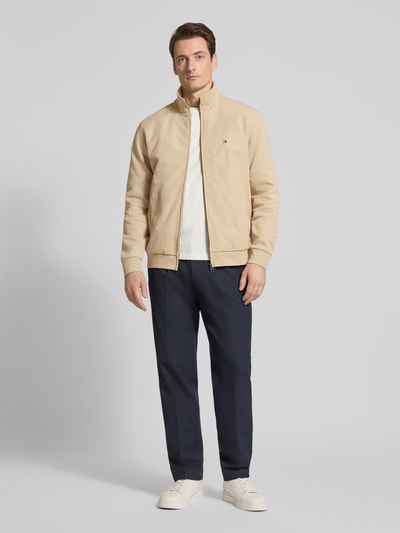 Männermodel trägt Regular Fit Blouson aus Baumwoll-Mix von Tommy Hilfiger in Beige mit Logo-Stitching, Ganzkörperansicht von vorne.