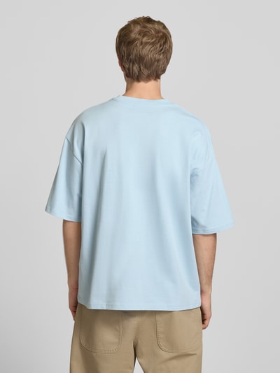 Mężczyzna model nosi Oversized T-Shirt mit Logo od REVIEW, czysta bawełna, oversize, jasnoniebieski kolor, widok całej sylwetki z tyłu.
