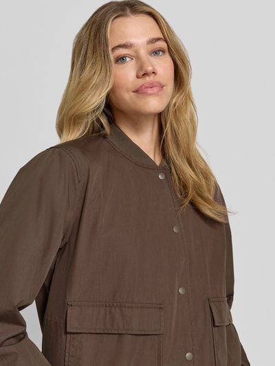 Modelka kobieca ma na sobie Jacke mit Pattentaschen od camel active, mieszanka bawełny, krój regular fit, stójka, listwa guzikowa, kieszenie z patką, brązowy kolor, tekstura gładka, szerokość ramion w rozmiarze 36: 43 cm, szerokość klatki piersiowej w rozmiarze 36: 55 cm, długość rękawów w rozmiarze 36: 58 cm, długość tyłu w rozmiarze 36: 54 cm, zbliżenie na górną część tułowia.