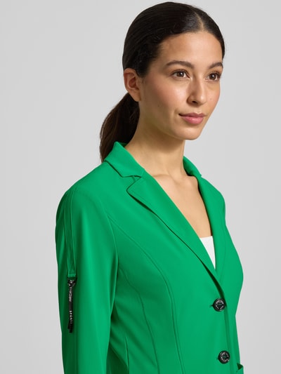 Kobiece modelka nosi Blazer mit Knopfverschluss von Marc Cain, zielony kolor, materiał z domieszką stretchu, krój slim fit, dekolt z klapami, długość tyłu w rozmiarze 36: 57 cm, szerokość w rozmiarze 36: 48 cm, długość rękawa w rozmiarze 36: 61 cm, zapięcie na guziki, kieszenie. Zbliżenie na górną część ciała z przodu.