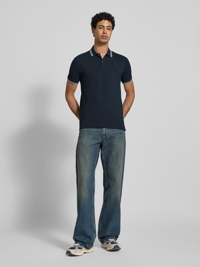 Männermodel trägt Slim Fit Poloshirt mit Logo-Stitching Modell 'Dunda' von G-Star Raw aus elastischem Baumwoll-Mix, dunkelblau, Polokragen, Ganzkörperansicht von vorne.