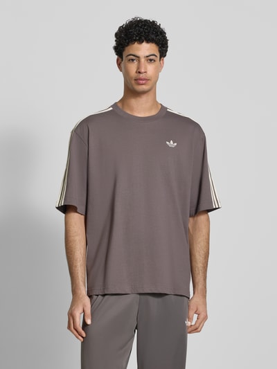 Mannelijk model draagt T-Shirt met Label-Stitching van adidas Originals in bruin, losse fit, geribde ronde hals, katoen, vooraanzicht bovenlichaam.