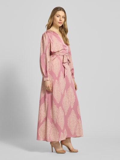Modelka nosi Regular Fit sukienka wieczorowa z nadrukiem paisley model 'Bretti' od Neo Noir, satyna, różowy i kremowy, styl kopertowy, z długim rękawem, z materiałową tasiemką, taliowany krój, dekolt w serek, zakończenia rękawów wykończone, Szerokość w rozmiarze 36: 48 cm, długość tyłu: 131 cm, długość rękawów: 63 cm, widok całej sylwetki z przodu.