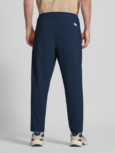 Männermodel trägt Relaxed Fit Bundfaltenhose mit Viskose-Anteil Modell 'VIGGO CROPPED' von Marc O'Polo Denim in Dunkelblau, elastischer Bund, Gesäßtaschen, Optik: Unifarben, Material-Mix mit Viskose-Anteil, Ganzkörperansicht Rückansicht.