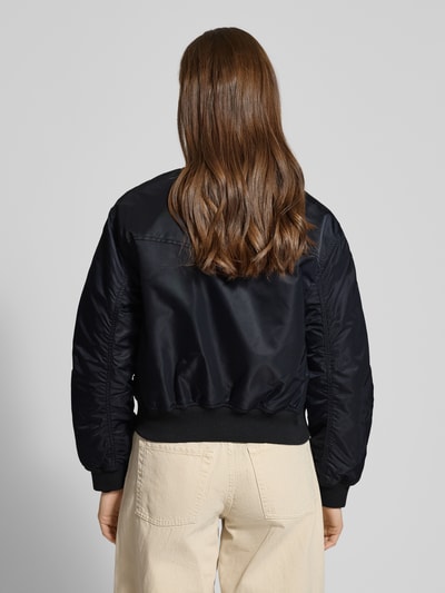 Frauenmodel trägt Bomberjacke mit Stehkragen und Reißverschluss Modell 'SCOUT' von Levi's®, schwarze glatte Struktur, Ganzkörperansicht Rückansicht. Regular Fit, Pattentaschen, Rückenlänge 50 cm, Schulterbreite 42 cm, Brustweite 40 cm, Ärmellänge 59 cm.