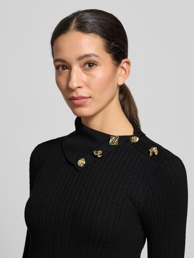 Frauenmodel trägt Slim Fit Rollkragenpullover aus Viskose-Mix Modell 'Sicilla' von Guess, schwarze Strick-Optik mit Zierbesatz, Nahaufnahme Oberkörper.