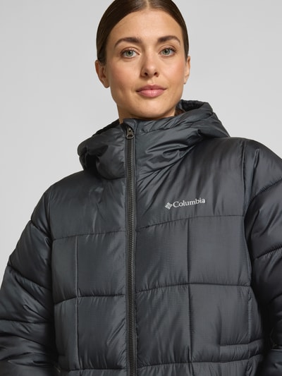 Kobiece modelka nosi Steppmantel mit Kapuze Modell 'Puffect III' von Columbia w kolorze ciemnoszarym, krój regular fit, tekstura pikowana, zamek dwukierunkowy, nadruk z logo, kieszenie na suwak, zbliżenie na górną część ciała.