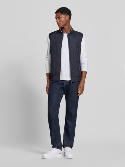 Männermodel trägt Regular Fit Weste in Stepp-Optik von Christian Berg Men, dunkelblau, Kombi mit Jeans, Ganzkörperansicht von vorne.