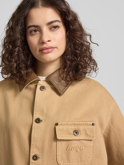 Frauenmodel trägt Regular Fit Jeansjacke aus reiner Baumwolle Modell 'FLIMANE-1-D_B' von Hugo Blue in Beige mit Umlegekragen und Brusttasche, Denim-Struktur, Nahaufnahme Oberkörper.