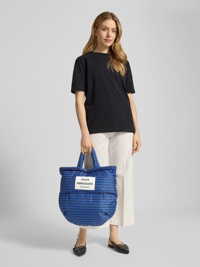 Frauenmodel trägt Handtasche mit Steppnähten und Label-Detail von MADS NØRGAARD im Allover-Look in Blau mit schwarzen Streifen, Ganzkörperansicht von vorne.