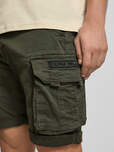 Mężczyzna nosi Shorts mit Cargotaschen Modell 'CREW SHORT' von Alpha Industries, bawełniano-elastanowy materiał, krój regular fit, kieszenie cargo, oliwkowa zieleń, szerokość w rozmiarze 32: 44 cm, długość nogawki wewnętrznej: 22 cm, zbliżenie na udo z boku
